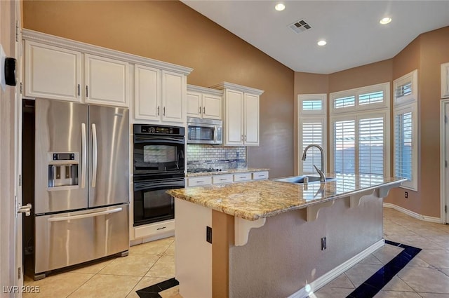 kitchen with sink, light stone counters, tasteful backsplash, a kitchen island with sink, and appliances with stainless steel finishes