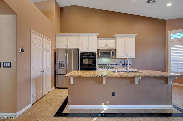 kitchen featuring light stone countertops, stainless steel appliances, an island with sink, a breakfast bar area, and sink