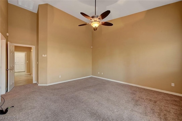 spare room featuring a towering ceiling, ceiling fan, and light colored carpet