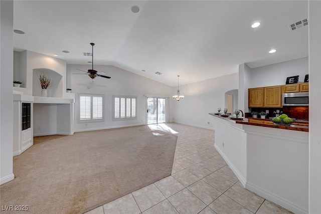 carpeted living room with vaulted ceiling and ceiling fan with notable chandelier