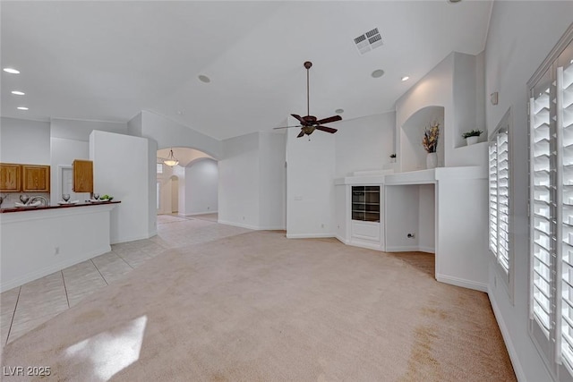 unfurnished living room with high vaulted ceiling, light carpet, and ceiling fan