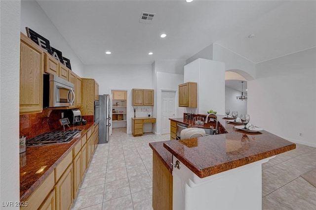 kitchen with appliances with stainless steel finishes, a kitchen bar, kitchen peninsula, and light tile patterned floors