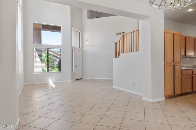 unfurnished room featuring a towering ceiling, an inviting chandelier, and light tile patterned floors