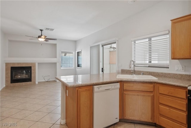 kitchen featuring kitchen peninsula, light tile patterned floors, white dishwasher, a fireplace, and sink