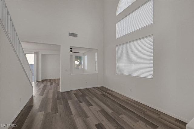 empty room with a towering ceiling, ceiling fan, and dark hardwood / wood-style flooring