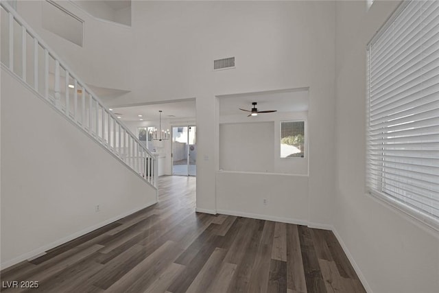 unfurnished living room featuring a towering ceiling, dark wood-type flooring, and ceiling fan with notable chandelier