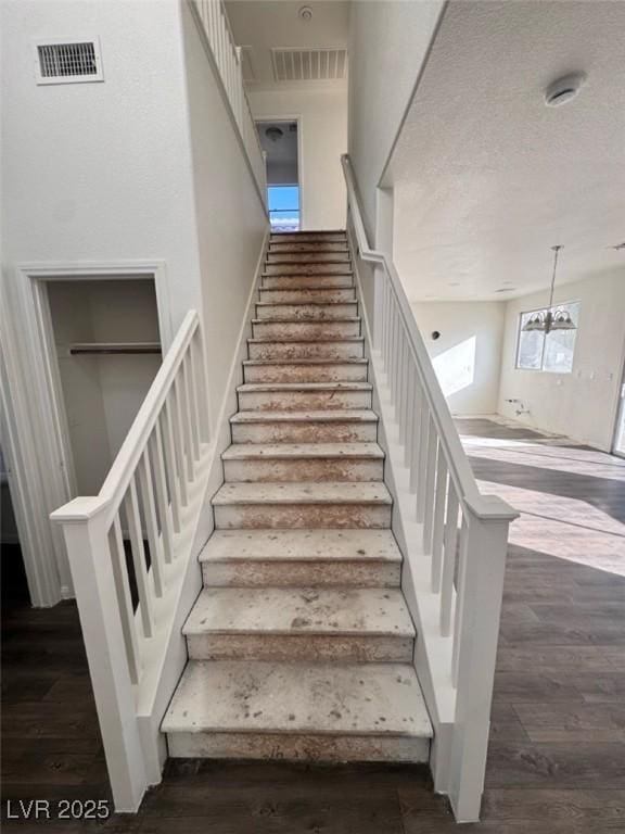 staircase featuring hardwood / wood-style flooring, an inviting chandelier, and a textured ceiling