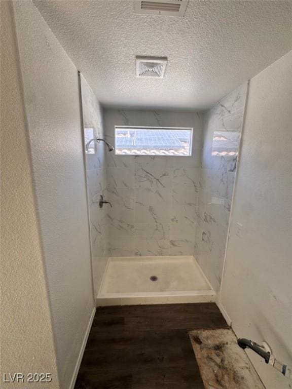 bathroom with a textured ceiling, a tile shower, and hardwood / wood-style floors