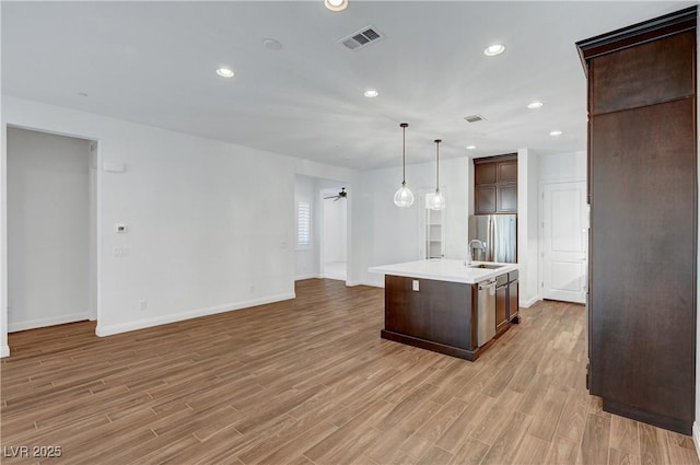 kitchen with ceiling fan, light hardwood / wood-style floors, stainless steel fridge, and an island with sink