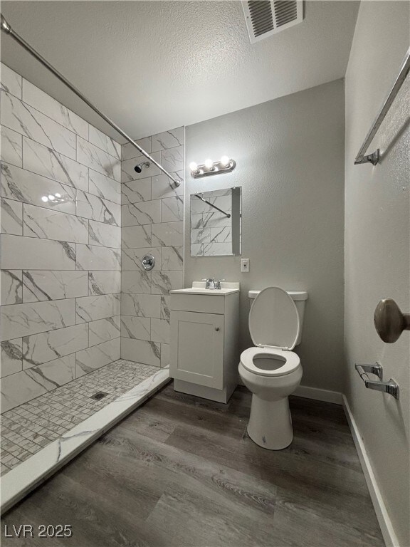 bathroom with a textured ceiling, a tile shower, wood-type flooring, and vanity