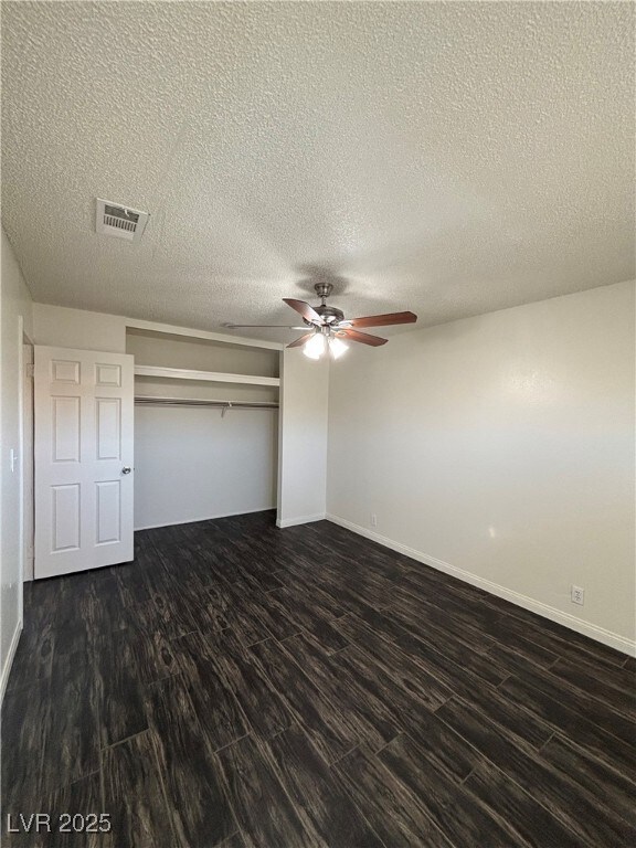 unfurnished bedroom featuring a closet, ceiling fan, a textured ceiling, and dark wood-type flooring