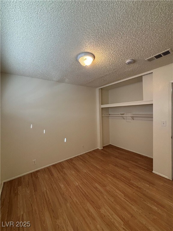 unfurnished bedroom with a textured ceiling, a closet, and wood-type flooring