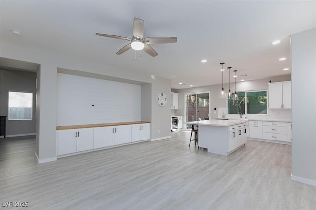 kitchen with white cabinetry, ceiling fan, light hardwood / wood-style floors, a kitchen island, and pendant lighting