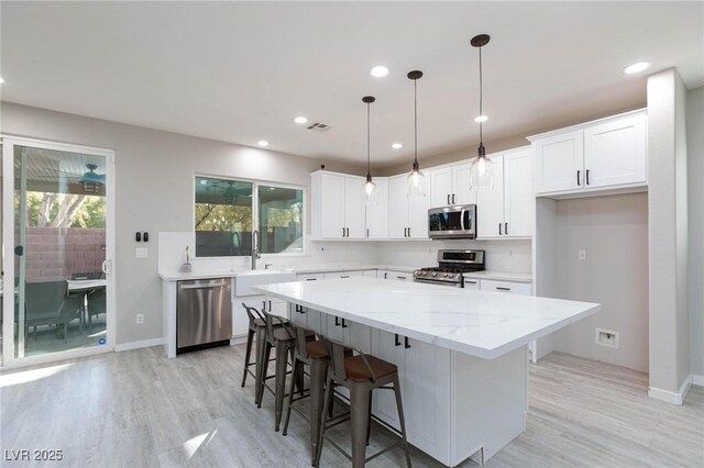 kitchen featuring hanging light fixtures, a center island, stainless steel appliances, white cabinetry, and sink