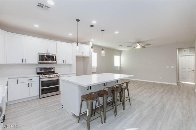 kitchen featuring stainless steel appliances, ceiling fan, pendant lighting, a kitchen island, and white cabinetry