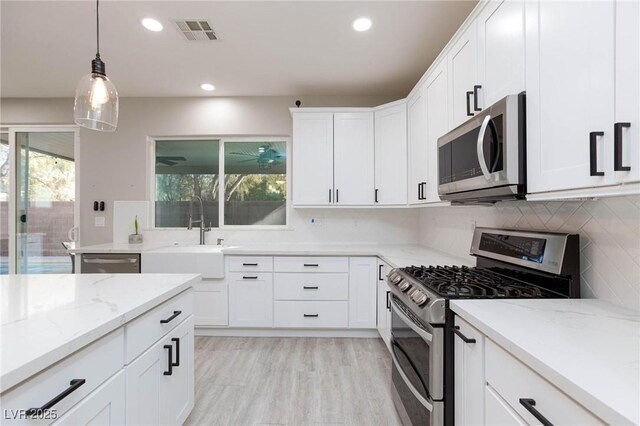 kitchen featuring stainless steel appliances, sink, decorative light fixtures, white cabinetry, and light stone counters