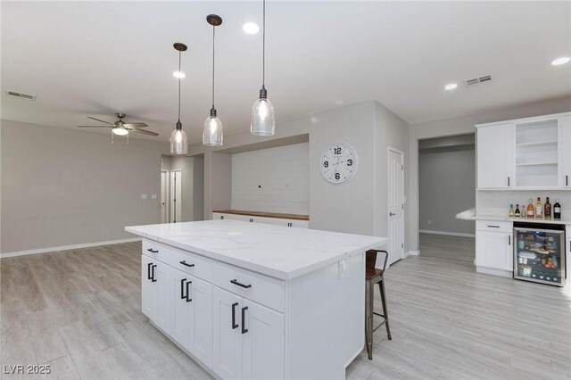 kitchen featuring white cabinets, a center island, ceiling fan, beverage cooler, and hanging light fixtures