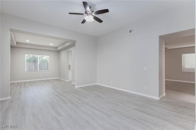 empty room with ceiling fan, light wood-type flooring, and a raised ceiling