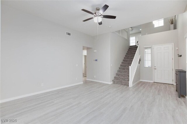 unfurnished living room with a high ceiling, ceiling fan, and light wood-type flooring