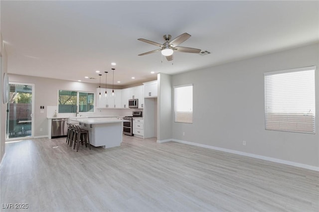 kitchen featuring stainless steel appliances, decorative light fixtures, a center island, white cabinetry, and light wood-type flooring