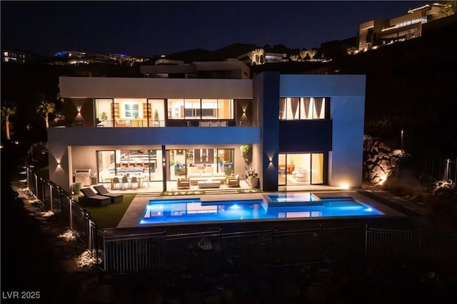 back house at night with a balcony, a pool with hot tub, a patio, and an outdoor living space