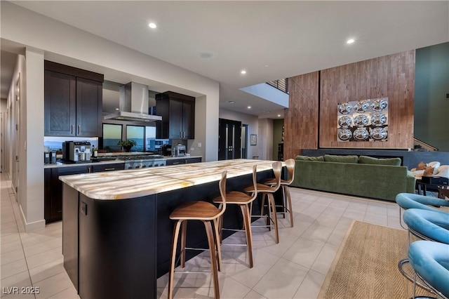 kitchen featuring a breakfast bar, a center island, wall chimney range hood, and light tile patterned floors