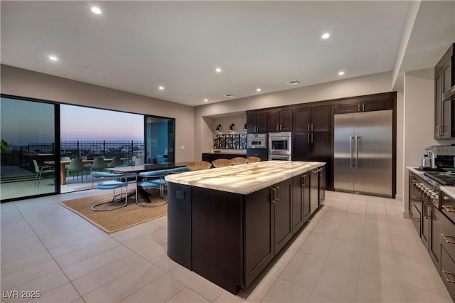 kitchen featuring appliances with stainless steel finishes, light tile patterned flooring, dark brown cabinets, and a center island