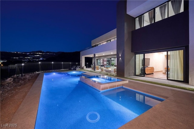 pool at night with a patio and an in ground hot tub