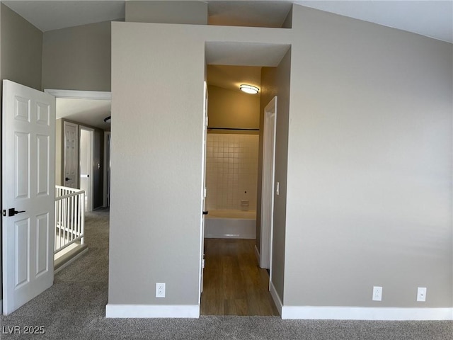 hallway with lofted ceiling and dark colored carpet