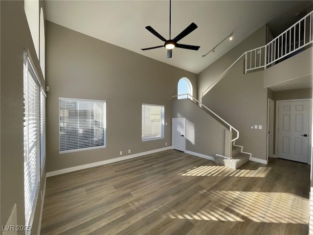 unfurnished living room featuring a towering ceiling, rail lighting, ceiling fan, and dark hardwood / wood-style flooring