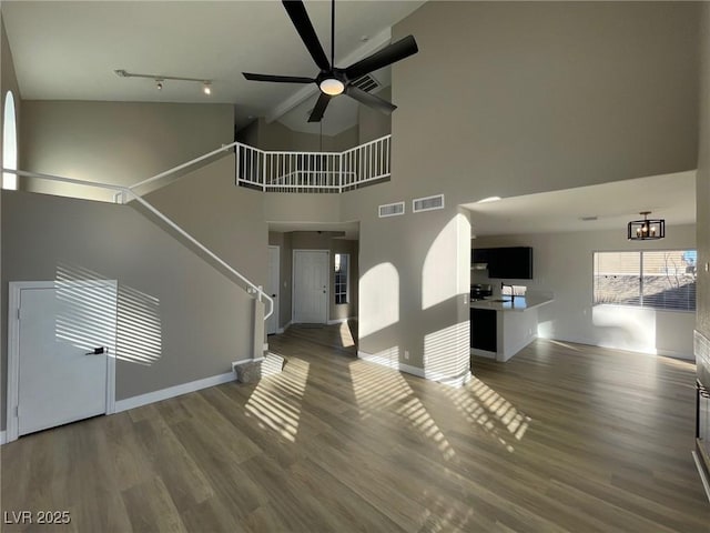 unfurnished living room with a towering ceiling, rail lighting, ceiling fan, and dark hardwood / wood-style flooring