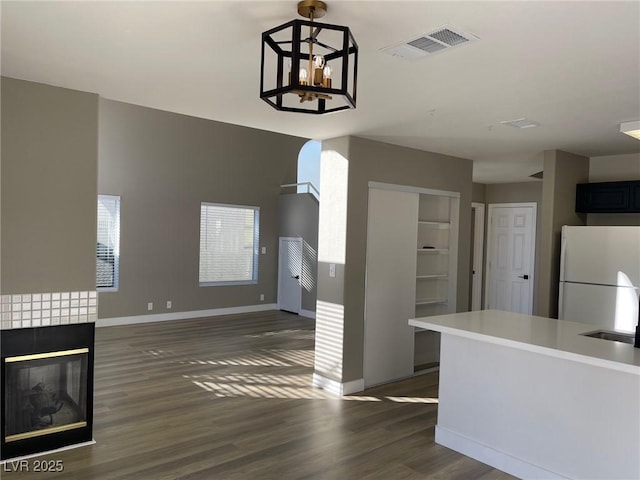 kitchen featuring a fireplace, white fridge, hanging light fixtures, a chandelier, and dark wood-type flooring