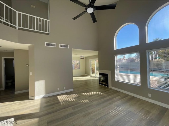 unfurnished living room featuring a towering ceiling, hardwood / wood-style floors, and ceiling fan