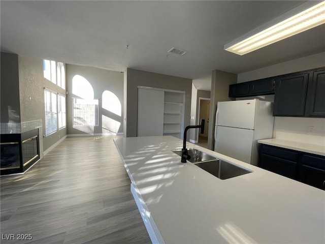 kitchen featuring sink, white fridge, hardwood / wood-style floors, and a large fireplace