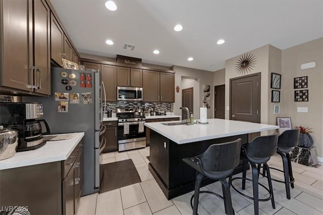 kitchen featuring stainless steel appliances, a sink, light countertops, a kitchen bar, and a center island with sink