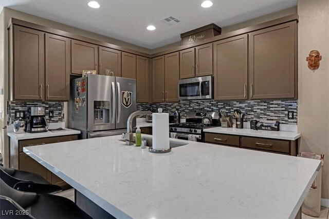 kitchen with a breakfast bar, stainless steel appliances, visible vents, a sink, and an island with sink