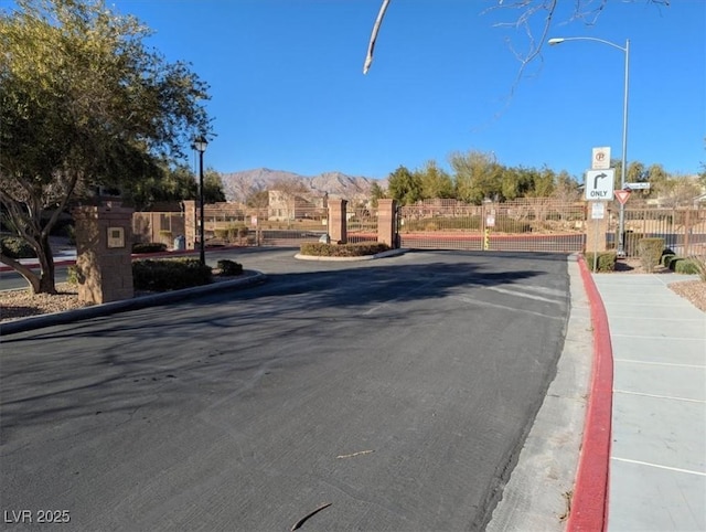 view of road with street lighting, a gate, a mountain view, a gated entry, and curbs