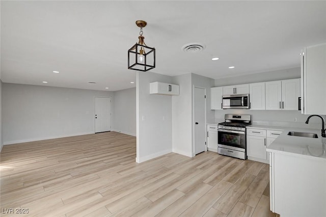 kitchen with pendant lighting, stainless steel appliances, light hardwood / wood-style floors, white cabinets, and sink