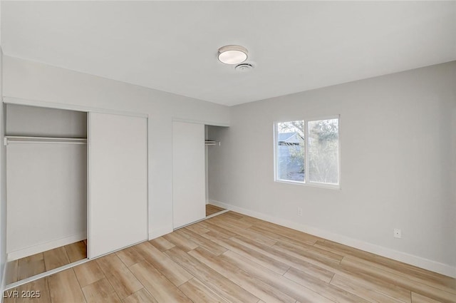 unfurnished bedroom featuring two closets and light hardwood / wood-style floors