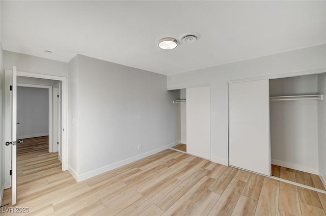 unfurnished bedroom featuring two closets and light wood-type flooring