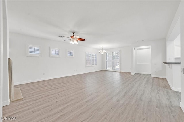 unfurnished living room with ceiling fan with notable chandelier and light hardwood / wood-style floors