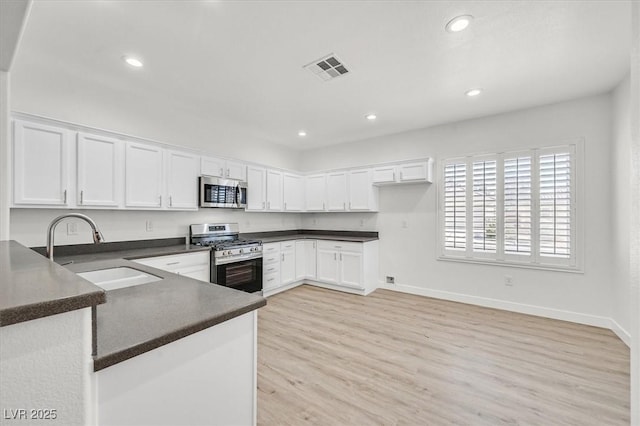 kitchen with appliances with stainless steel finishes, light wood-type flooring, white cabinets, and sink