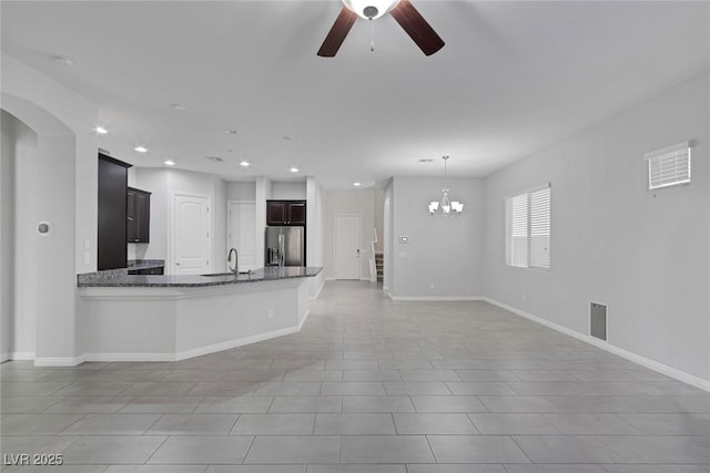 kitchen featuring ceiling fan with notable chandelier, stainless steel refrigerator with ice dispenser, dark stone counters, sink, and kitchen peninsula