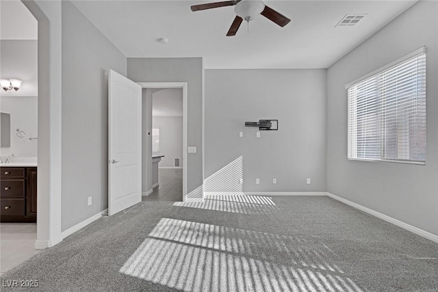 unfurnished bedroom featuring ceiling fan, light colored carpet, and ensuite bath