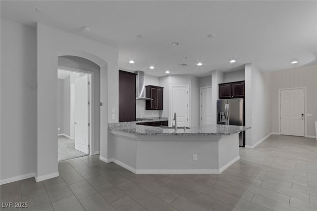 kitchen featuring kitchen peninsula, sink, stainless steel appliances, wall chimney exhaust hood, and light stone counters