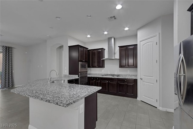 kitchen featuring kitchen peninsula, stainless steel appliances, wall chimney exhaust hood, dark brown cabinetry, and sink