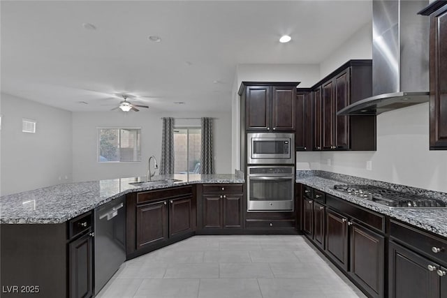 kitchen with ceiling fan, sink, light stone countertops, stainless steel appliances, and wall chimney exhaust hood