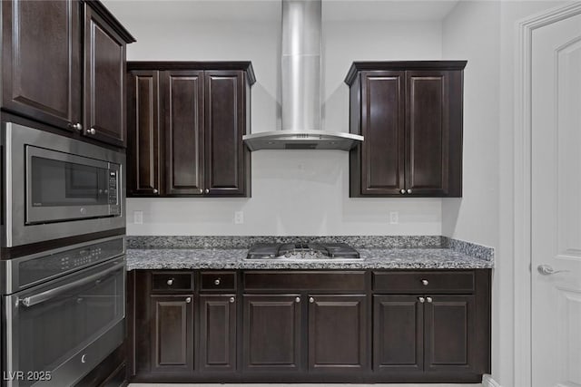 kitchen with appliances with stainless steel finishes, wall chimney range hood, stone countertops, and dark brown cabinets