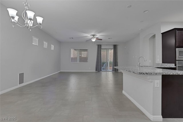 kitchen featuring ceiling fan with notable chandelier, stainless steel appliances, sink, hanging light fixtures, and light stone counters