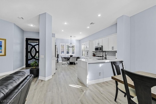 kitchen with white cabinets, light hardwood / wood-style flooring, hanging light fixtures, and kitchen peninsula